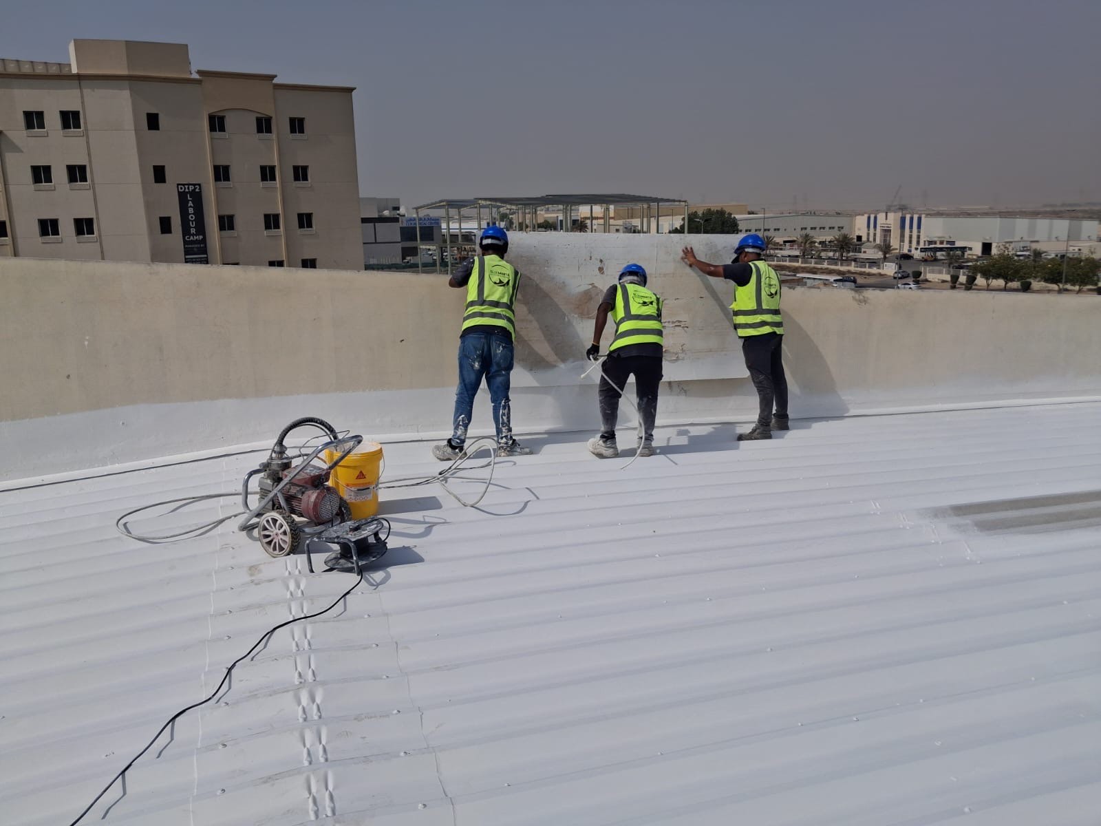 CoolRoof UAE crew treating the parapet junction on the warehouse roof